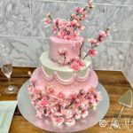 Pink and white floral wedding cake on a wooden table.
