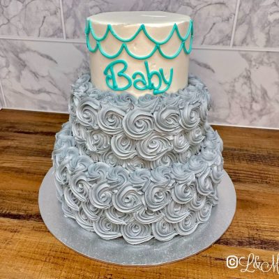 Three tier silver baby shower cake on a wooden table.