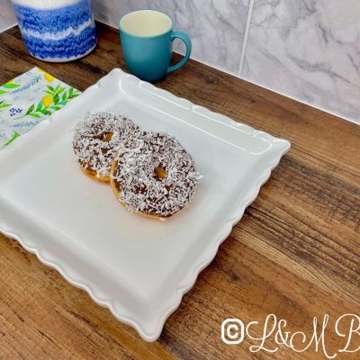 Chocolate donut with coconut flakes on a white serving tray.