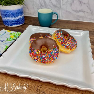 Chocolate donut with sprinkles on a white tray.