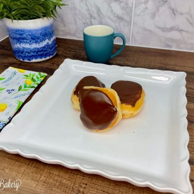 Custard donut with chocolate icing on a white serving tray.