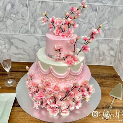 Pink and white floral wedding cake on a wooden table.