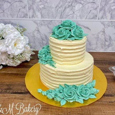Wedding cake with teal flowers on a wooden table.